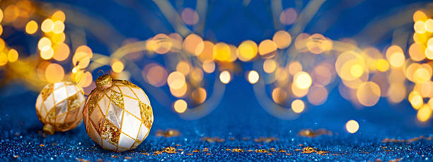 istock Elegant gold baubles resting on blue glitter surface with warm bokeh Christmas lights. Christmas, Winter or New Year concept 2241773449