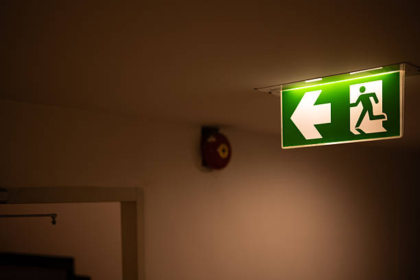 istock Exit way arrow direction guidance sign green color light emergency exit sign in a dark room 2241773660