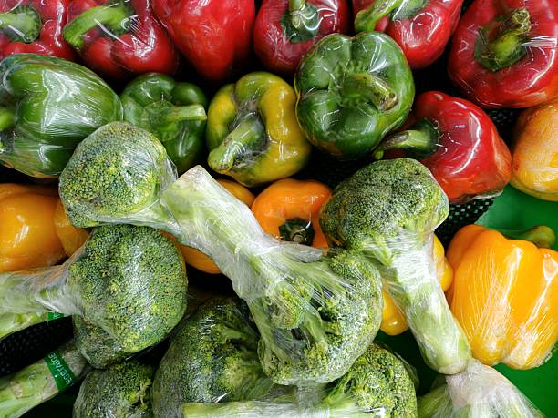 Close-up, full-frame view of colorful broccoli and mixed capsicum (bell peppers) tightly packed and individually wrapped in plastic packaging