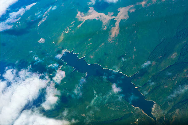 Winding lake nestles between forested mountains, its irregular shoreline dotted with peninsulas and inlets. Wisps of cloud drift above the dense greenery, adding depth to the aerial perspective