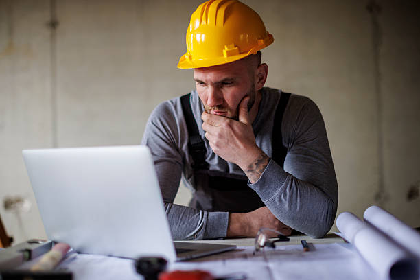 istock Focused construction worker reviewing construction plans on laptop 2241780407