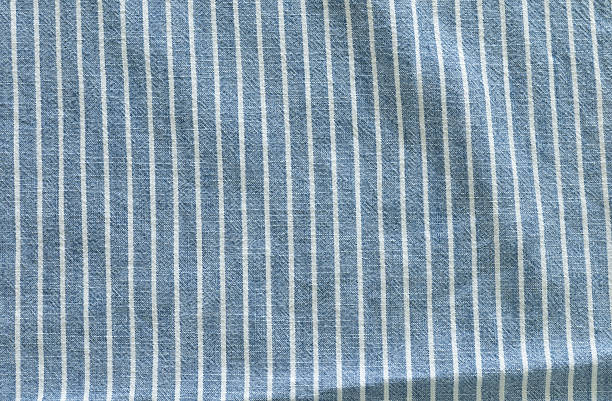 istock Top view, close-up of a blue fabric with thin, vertical white stripes. The image highlights the linear pattern and the texture of the woven material, with some gentle folds. 2241784413