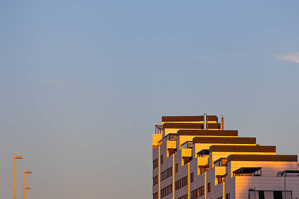 Madrid. Spain. Modern terraced residential building with geometric balconies glowing in warm golden-hour light against a clear blue sky