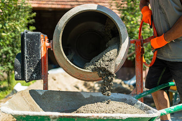 istock Construction worker pouring fresh concrete from a cement mixer into a wheelbarrow at a building site 2241795492