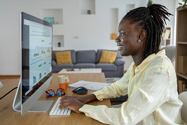 istock Cheerful black woman working on her computer from home with a graphs visible on the screen of the monitor 2241801502