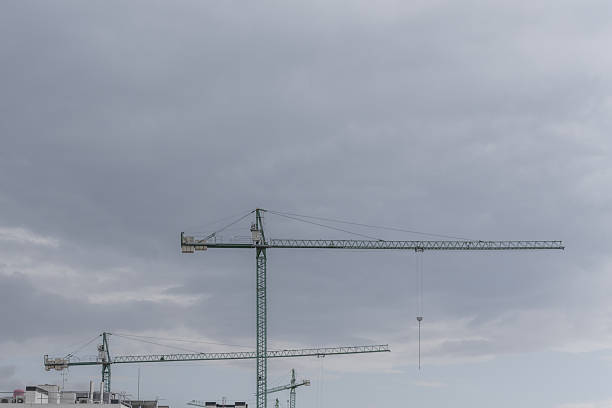 Green cranes with concrete counterweights for the construction of buildings on a day with heavy rainy skies