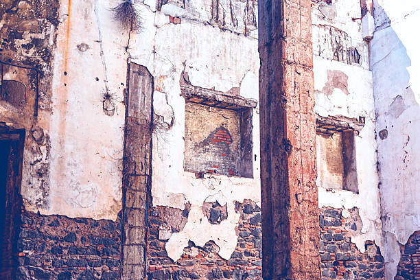 Weathered facade of crumbling plaster exposes rustic bricks and sturdy wooden beams in shadowed alcove. Faded niches and a dark doorway whisper tales of abandonment and erosion. Weathered facade