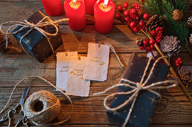 A cozy Christmas scene with red candles, a spool of natural jute twine, baubles and a wrapped present on a rustic wooden table. The soft glow of candlelight and handmade wrapping evoke feelings of warmth, mindfulness and sustainable holiday traditions. Copy space for text - Christmas, handcrafted