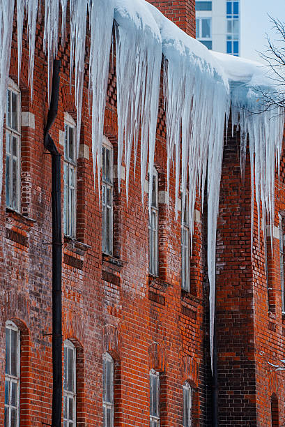 Icicles dangling from weathered brick facade, sharp crystalline forms highlighting winter's stark urban beauty and potential danger beneath glistening snow-laden surfaces