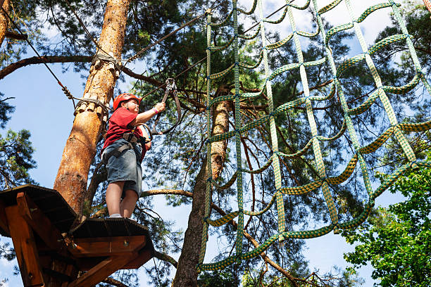 A child in red climbing on a rope adventure course in a forest with safety gear. Outdoor courage and adventure concept.