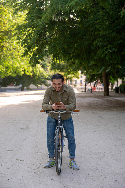 istock Asian man using phone on vintage bicycle in park 2241811974