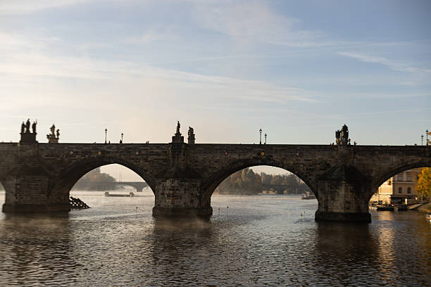 Prague, czech republic - october 14, 2025: charles bridge spanning the vltava river in prague, experiencing a misty morning with fog lifting from the water