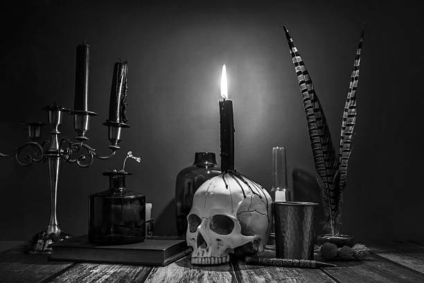 A black and white image of candles in a candelabra, a skull with drops of wax and vintage objects for scribes