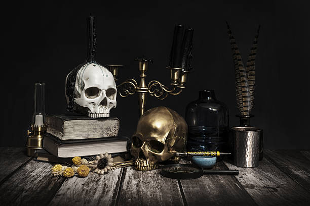 A frontal image of candles in a candlestick, some skulls with drops of cere, another of gold and vintage reading and writing objects