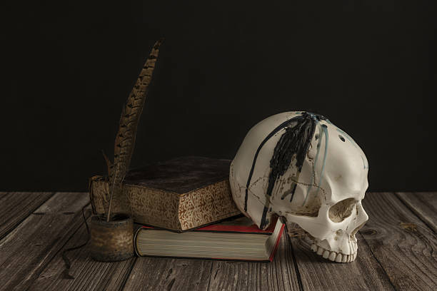 istock a white skull with teeth next to some old books and a pen to write with ink on a board 2241820163