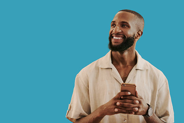 istock Smiling African American Man Holding Smartphone Against Blue Background Creative Expressions 2241828784