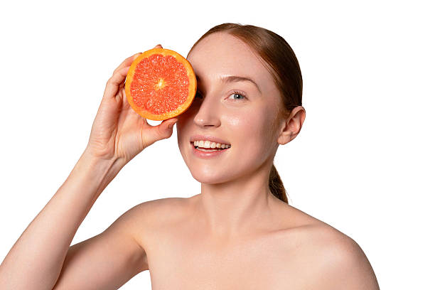 istock Woman holding a grapefruit slice near her face while smiling happily against a white background 2241828968