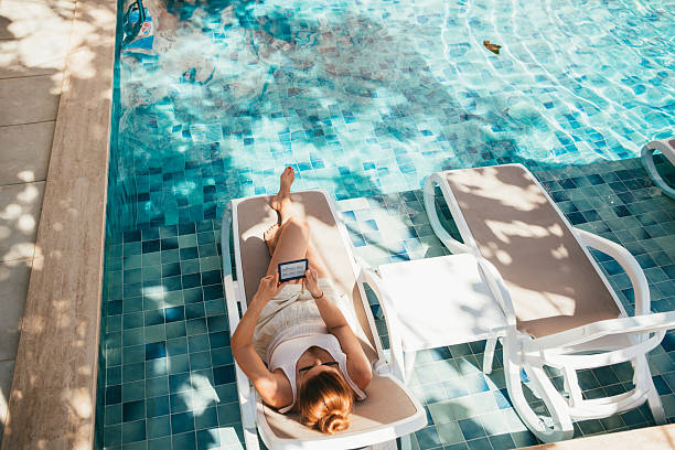 istock Relaxed young woman enjoying sunny poolside leisure while reading electronic book on lounger. Summer vacation mood, peaceful atmosphere, digital reading lifestyle slow living modern relaxation concept 2241836115