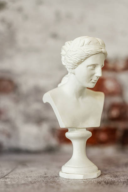 istock Small bust of classical Greek figure on gray background with half-bare bricks on the wall 2241849011