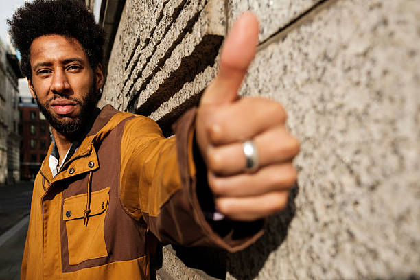 istock Young man showing thumbs up sign by concrete wall 2241854612