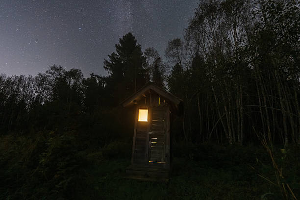 istock A mysterious light glows from a rustic wooden outhouse deep in a dark forest under a brilliant starry night sky. 2241867314