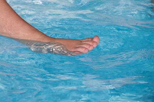 Close-up of a foot gently touching clear blue pool water, creating soft ripples and reflections. Concept for summer, relaxation, vacation, and leisure by the swimming pool.
