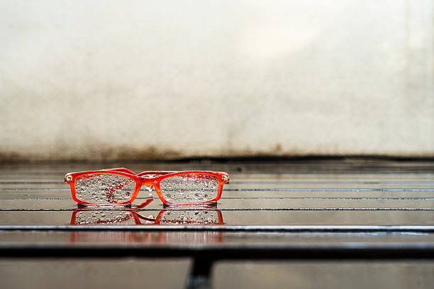 Wet orange-rimmed reading glasses on a floor of wet planks