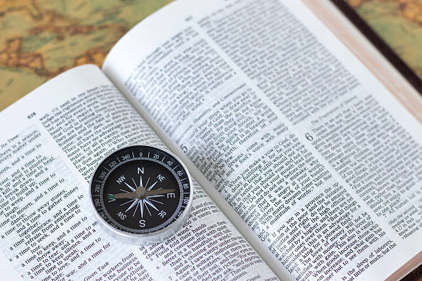 istock Compass on open holy bible book and ancient world map 2241883645