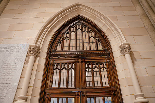This photo captures a richly detailed wooden door set within a pointed Gothic arch in a stone cathedral interior. The door features intricate carved patterns and glass panels, framed by ornate columns and masonry.
