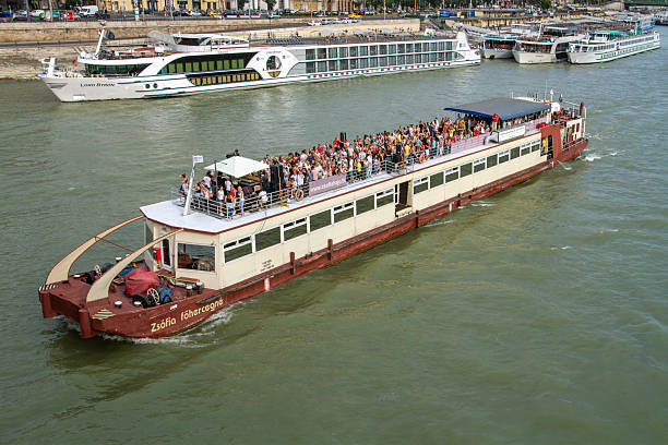 Budapest, Hungary: Crowded Tourist Sightseeing Boat with Passengers and Luxury River Cruise Ships on Danube River. Party ship in Budapest, Hungary