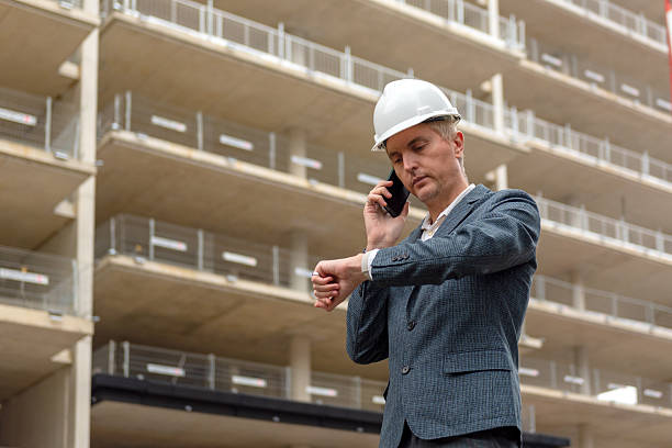 Construction manager checking time while on phone at building site outdoors. stock photo