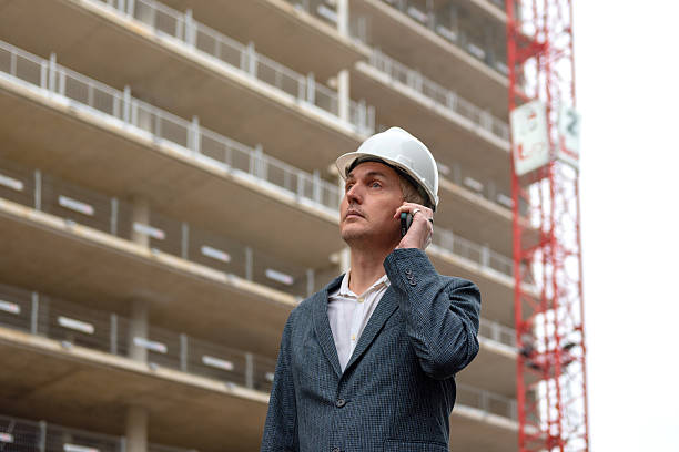 Construction manager in hard hat talking on phone at building site outdoors. stock photo