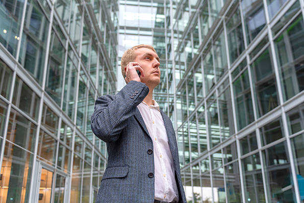 Businessman on phone surrounded by modern glass architecture outdoors. stock photo