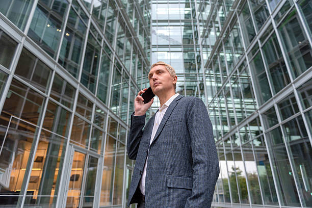 Businessman on phone surrounded by modern glass architecture outdoors. stock photo