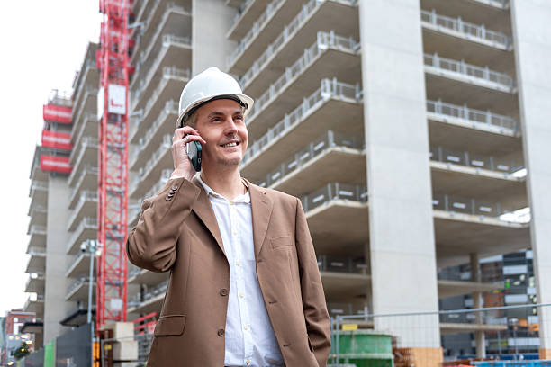 Smiling construction manager talking on phone at building site in city area. stock photo