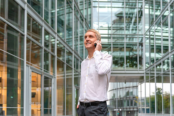 Businessman on phone surrounded by modern glass architecture outdoors. stock photo