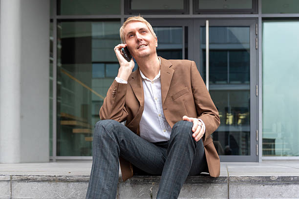 Businessman talking on smartphone while sitting on office steps outdoors. stock photo