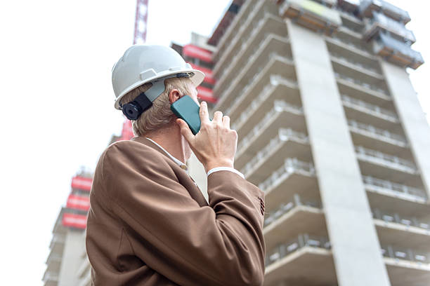 Engineer in hardhat talking on phone at construction site with high-rise building. stock photo