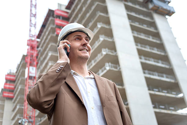 Smiling construction manager talking on phone at building site in city area. stock photo