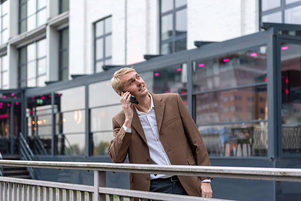 Businessman talking on smartphone near modern building with glass facade outdoors. stock photo