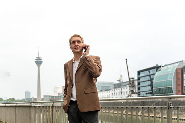 Businessman talking on phone near city riverwalk with modern buildings in background. stock photo