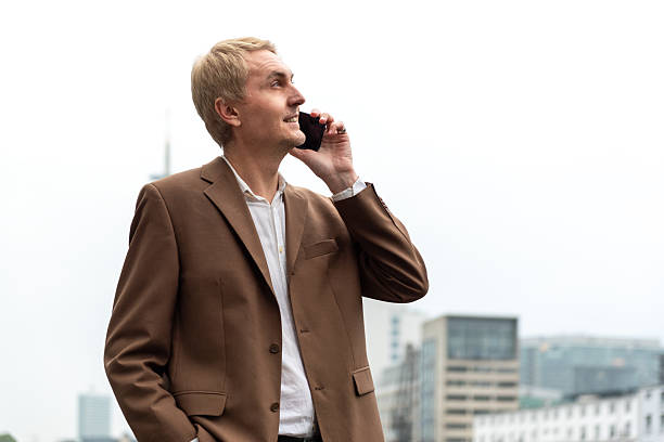 Businessman talking on phone near city riverwalk with modern buildings in background. stock photo