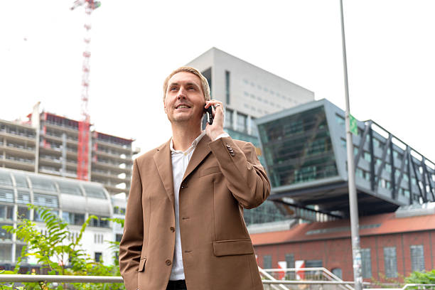 Businessman talking on phone near city riverwalk with modern buildings in background. stock photo