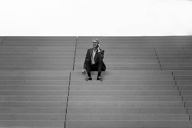 Businessman sitting on wide concrete steps talking on phone in black and white.. stock photo