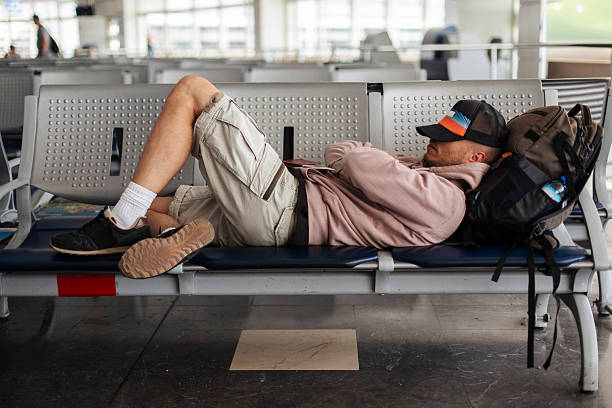 A tired traveler lounges on airport benches with a backpack, pausing during a layover; The scene conveys travel fatigue, rest, and everyday transit moments