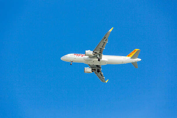 Underside view under below of a Pegasus Airlines aircraft operated by Turkey, captured mid-flight against a clear blue sky. The plane features a white fuselage with “flypgs.com” branding and a yellow tail fin with red “PEGASUS” lettering. The extended landing gear and clean composition highlight the aircraft’s structure and vibrant branding, ideal for aviation visuals and Turkish travel themes.