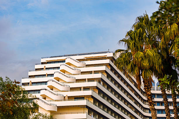 Contemporary multi-story hotel in Antalya, Turkey, featuring a white facade and staggered balconies that create a geometric visual rhythm. Surrounded by palm trees and bathed in clear daylight, the building blends Mediterranean climate with modern design. Ideal for visuals focused on coastal hospitality, architectural elegance, and upscale travel accommodations.