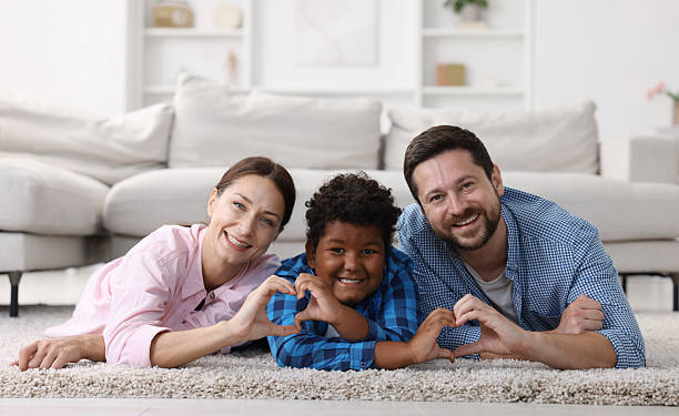 istock Adoption. Parents and their son making heart gestures on floor at home 2241904014