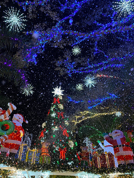 Bright Christmas display featuring Santa Claus and large illuminated tree under falling snow. Festive lights and decorations create a cheerful holiday atmosphere.