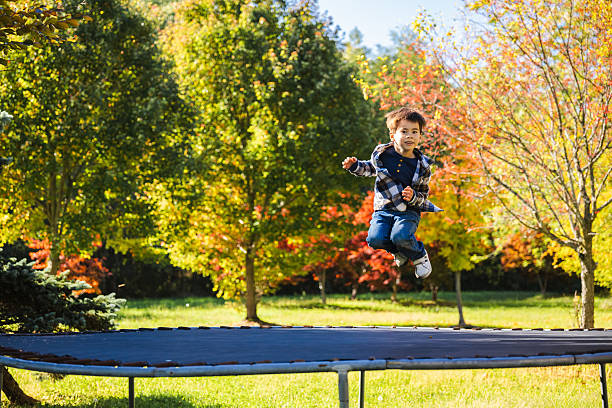 Happy boy jumping on a trampoline in the backyard surrounded by colorful autumn trees. High quality photo